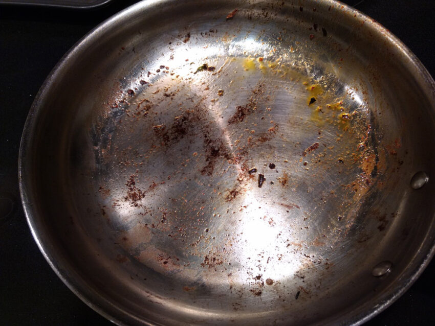 A stainless steel pan with oily brown residue stuck on the bottom