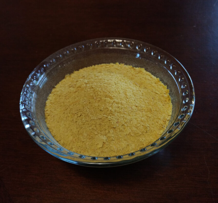 a small glass bowl of nutritional yeast flakes on a dark wood table