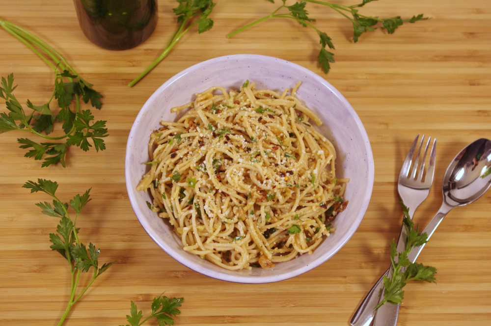 parsley sprigs surround a bowl of spaghetti speckled with herbs, chili flakes, and cheese