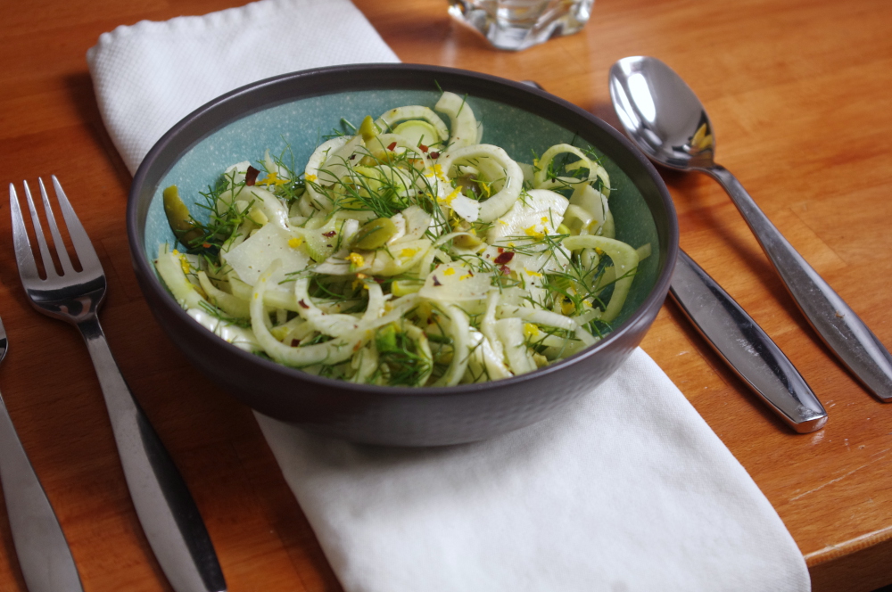 a place setting with a teal and gray bowl filled with curly green and white fennel salad