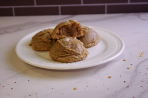 four cookies, one half eaten, on a white plate with chili flakes scattered around the marble countertop.